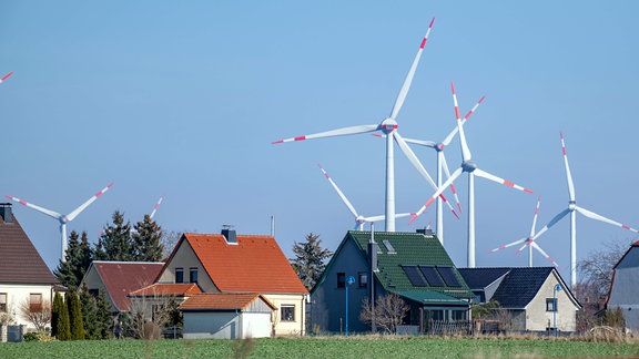 Windräder drehe sich hinter einer Siedlung mit Eigenheimen bei Wethau in Sachsen-Anhalt.