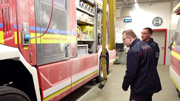 Zwei Feuerwehrmänner begutachten Schäden an einem Feuerwehrfahrzeug.