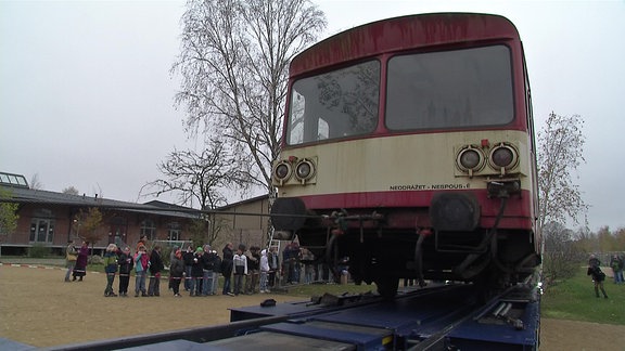 Schüler der Freien Waldorfschule Görlitz verfolgen, wie ein ausgedienter Eisenbahnwaggon von einem Tieflader auf ihren Schulhof entladen wird