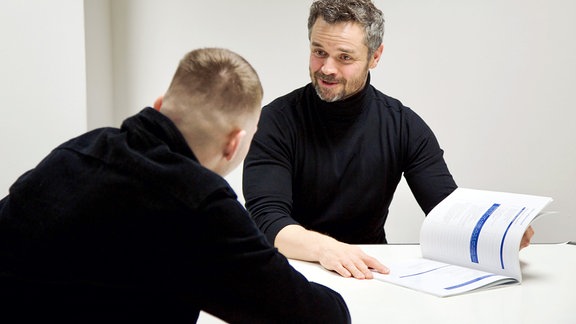 Zwei Männer im Gespräch an einem Tisch.