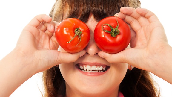 Lachendes Kind hält sich 2 Tomaten vor die Augen.