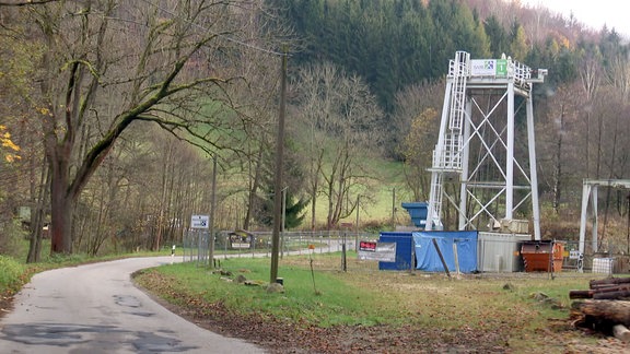 An einer kleinen Straße in einem Tal steht ein eingezäunter Förderturm.