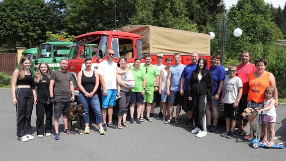 Viele Frauen, Männer und Kinder stehen vor Oldtimern und schauen in die Kamera. 