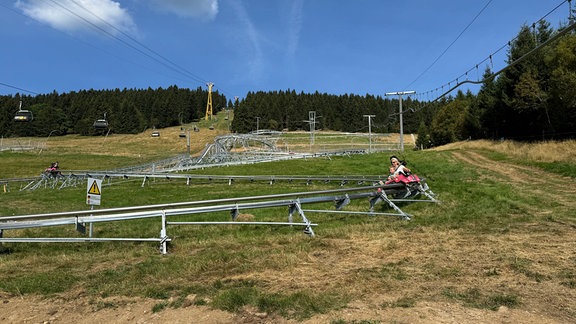 Eine Frau fährt auf einer geschwungenen Sommerrodelbahn den Berg hinunter.