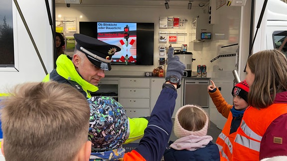 Ein Polizeibeamter erklärt einer Gruppe von Kindern Bahn-Verkehrszeichen.