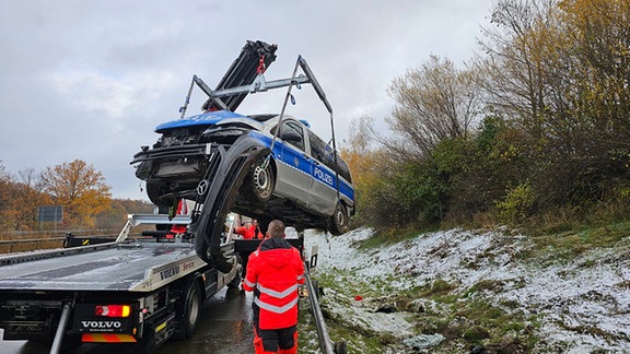 Ein beschädigter Streifenwagen wird auf einen Abschleppwagen gehoben.