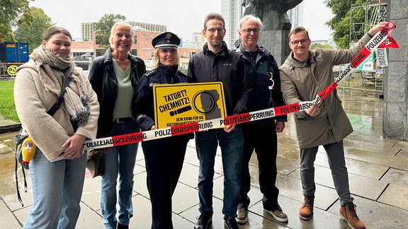 Menschen stehen mit einer Polizistin vor einem Absperrband