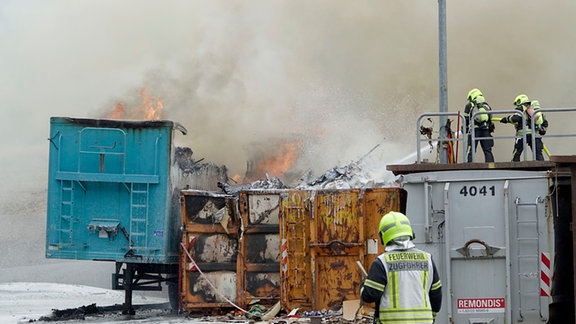 Feuerwehrleute in Schutzanzügen kämpfen mit Löschwasser aus Schläuchen gegen Flammen auf einer Mülldeponie.