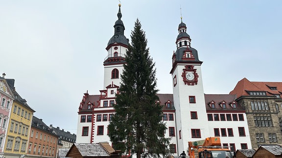 Zwischen den zwei Türmen des alten Rathauses von Chemnitz ragt der diesjährige Weihnachtsbaum in die Höhe. Daneben sind schon einige Weihnachtsmarktbuden aufgebaut, die aber noch geschlossen sind.  