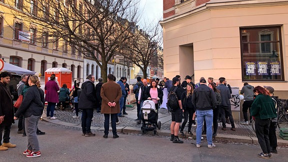 Menschen stehen vor einem Gebäude in Chemnitz und unterhalten sich in Gruppen.