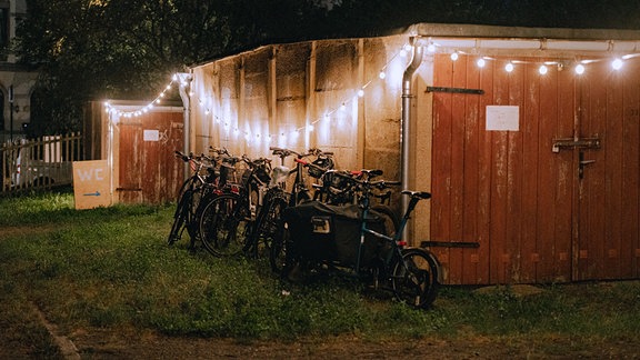 Fahrräder lehnen an einer Garagenwand am Abend, stimmungsvolle Lichterketten sind gespannt.