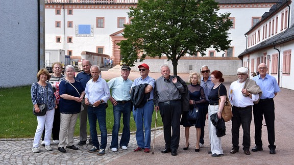 Eine Gruppe von fünf älteren Frauen und acht älteren Männern steht auf dem Vorhof von Schloss Augustusburg.