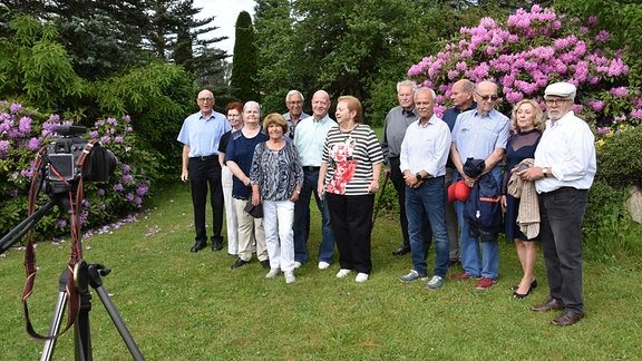 Eine Gruppe von älteren Frauen und Männern steht beim Klassenfoto in einem Park.