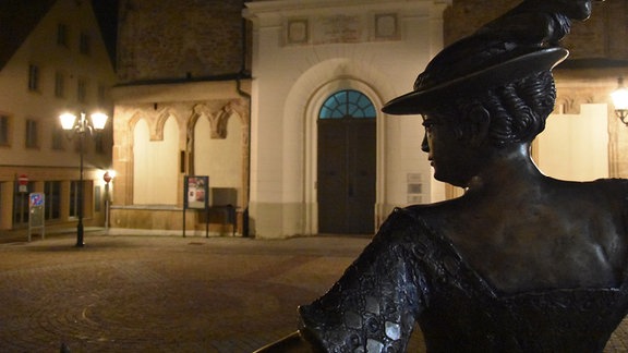 Blick über eine Steinfigur zur nächtlich erleuchteten Freiberger Nikolaikirche.