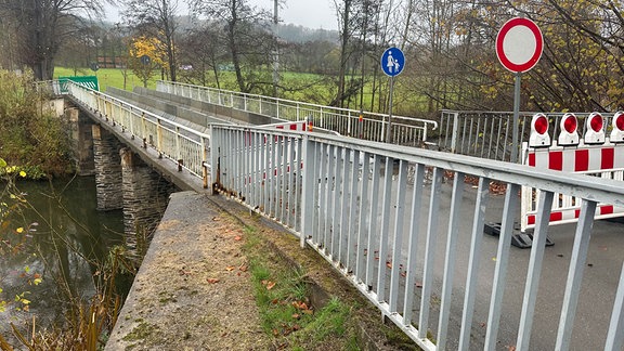 Blick seitliche auf eine schmale Brücke. Die Überfahrt ist abgesperrt mit Gittern. Das Geländer ist stark angerostet. Das Mauerwerk der Stützpfeiler sieht historisch aus. 