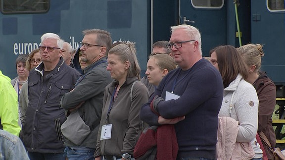 Blick auf eine stehende Zuschauergruppe. An den Gesichtern der meisten ist zu erkennen, das sie ziemlich bewegt sind. 