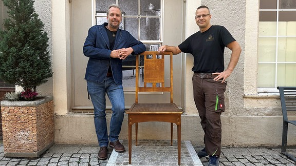 Zwei Männer stehen an einem Stuhl-Denkmal in Zschopau. 