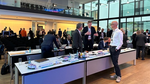 Viele Männer stehen und sitzen bei einem Automobilkongress in einer Kongresshalle.