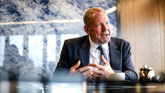 Frank Richter, ein Mann sitzt an einem Schreibtisch, hinter ihm ein großes Bild mit Wolken