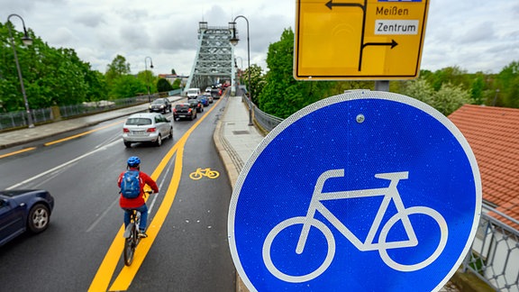 Ein Radfahrer fährt an der Elbbrücke Blaues Wunder auf einem markierten Radweg. 