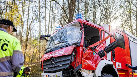 Ein recht neues Spezialfahrzeug der Feuerwehr lsteht auf der Straße und ist auf der linken Seite toal demoliert. Die Fronstscheibe ist zersplittert.