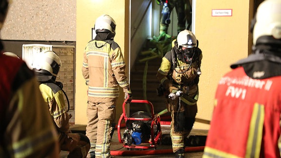 Feuerwehrleute kommen nach einem Löscheinsatz aus dem Eingang eines Wohnblocks.