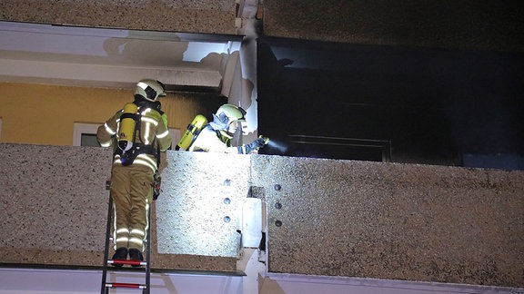 Feuerwehrleute klettern mit einer Leiter zum Balkon einer brennenden Wohnung.