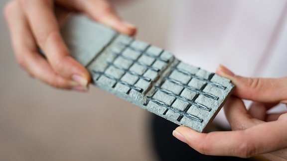 Eine Frau zeigt eine dünne Platte aus einem Beton-Verbundwerkstoff 