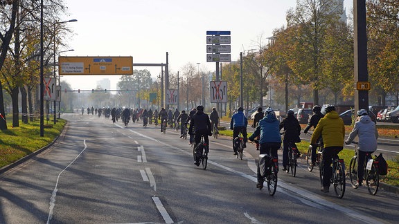 Eine breite urbane Straße ist frei von Autos. Auf ihr fährt eine große Kolonne von Fahrrädern.