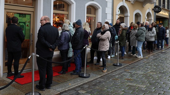 30, 40 Menschen stehen bei Nieselregen in einer Schlange vor einem Geschäft in Dresden,