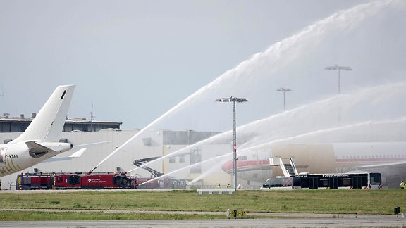 Feuerwehrautos bespritzen ein Flugzeug mit Wasser.