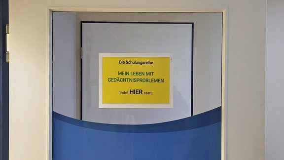 Schild an einer Tür mit der Aufschrift: "Schulungreihe - Mein Leben mit Gedächtnisproblemen - findet hier statt"