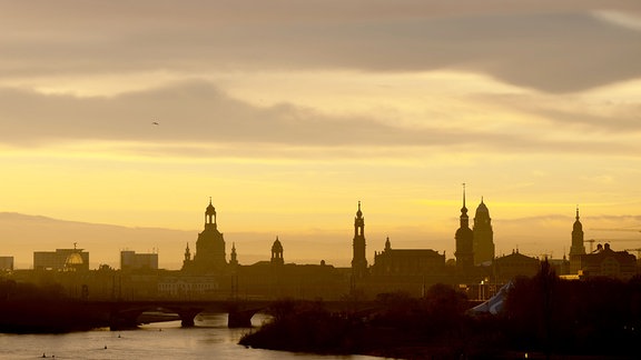 Die Kulisse der Altstadt mit der Frauenkirche (l-r), dem Ständehaus, der Katholischen Hofkirche, dem Hausmannsturm, dem Rathausturm und der Kreuzkirche zeichnen sich bei Sonnenaufgang als Silhouette ab.