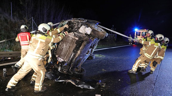 Einsatzkräfte der Feuerwehr stellen einen demolierten Kleinbus wieder auf seinen Räder.