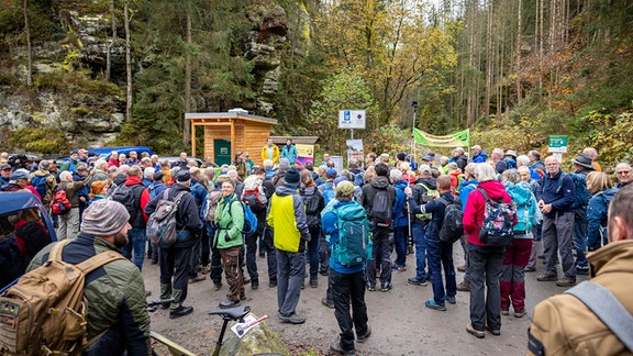 Eine große Gruppe Menschen versammelt sich mitten im Wald. 