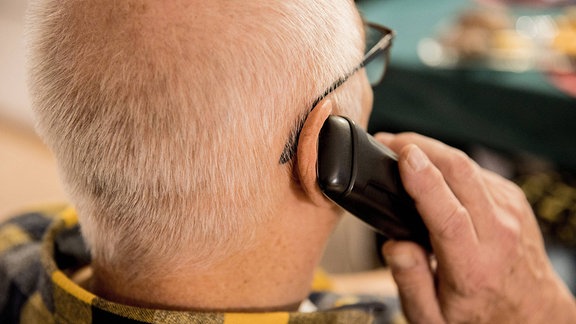 Ein älterer Mann sitzt in seiner Wohnung und telefoniert