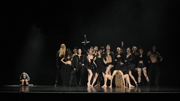 Szene aus dem Tanztheaterstück "Wonderful World": Tänzerinnen und Tänzer in knappen, schwarzen Party-Outfits tanzen auf einer Bühne.