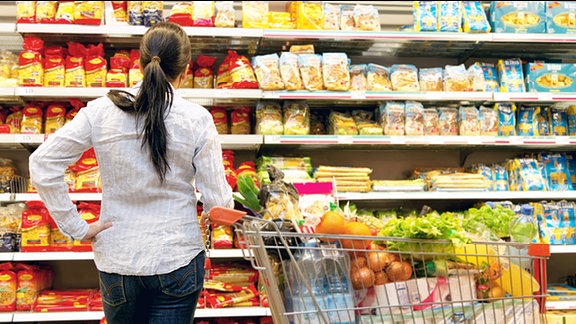 Eine junge Frau steht mit einem vollen Einkaufswagen vor einem Supermarktregal