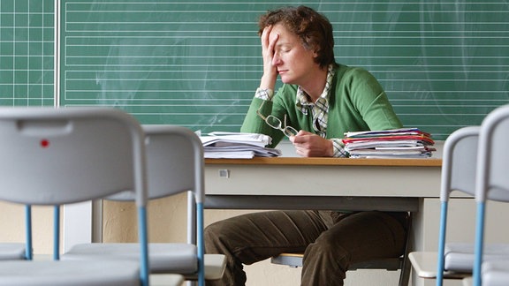 Lehrerin sitzt alleine in einem Klassenraum