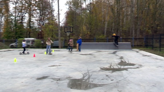 Kinder und Jugendliche fahren auf einer Skate-Anlage.