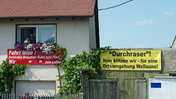 Ein Mann gießt seine Blumen über einem Transparent mit der Aufschrift "Fahrt leise! Behörden brauchen Ruhe zum Planen. Wir brauchen Ruhe zum Leben!" in der Ortschaft Wellaune (Kreis Nordsachsen), aufgenommen 06.07.2011. Die Gemeinde kämpft seit neun Jahren für einen Ortsumgehung. Gleich drei Bundesstraßen führen durch den Ort.