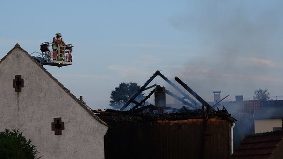 Ein Feuerwehrmann stehe auf der Drehleiter an einem verkohlten Dachstuhl.