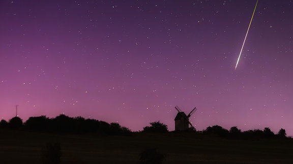 Silhouette einer Mühle vor rosa Polarlicht und einer fallenden Sternchnuppe