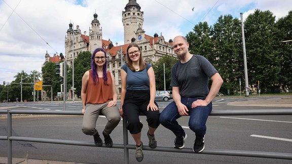 Verein aus Leipzig gegen Fake News: Drei Menschen sitzen auf einem Geländer an einer großen Kreuzung vor dem Neuen Rathaus in Leipzig.