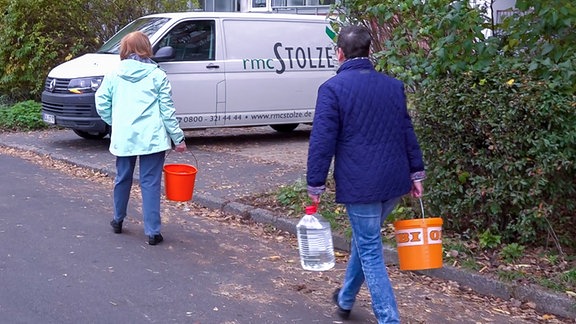 2 Frauen tragen Wasserkanister in eine großes Wohnhaus.