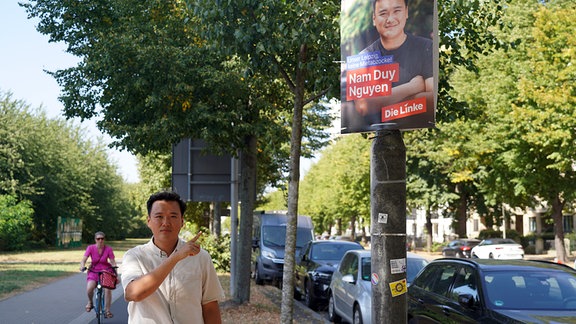 Nam Duy Nguyen zeigt auf sein Wahlplakat in seinem Wahlbezirk