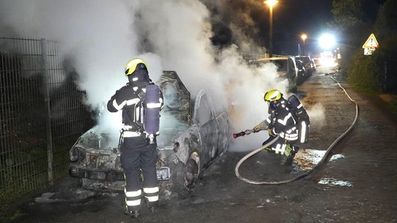 Zwei Autos in Leipzig wurden offenbar abgebrannt: Zwei Feuerwehrleute löschen ein ausgebranntes Auto.