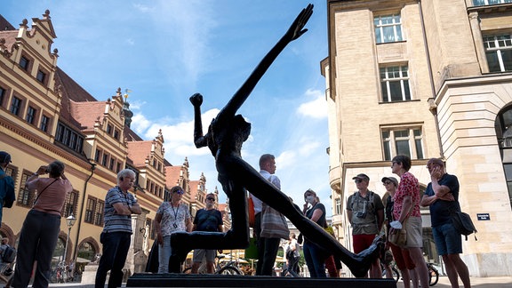 Skulptur Der Jahrhunderschritt in der Leipziger Innenstadt: Eine Metallfigur mit ausgestrecktem rechten Arm und Bein, das linke Bein kniet, die linke Gand ist zur Faust geballt