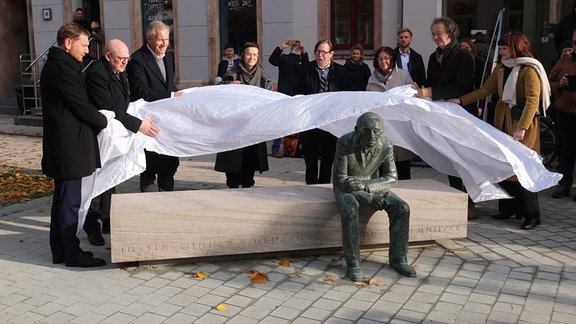 Michael Kretschmer (CDU, l-r), Ministerpräsident des Landes Sachsen, Sven Schulze (SPD), Oberbürgermeister von Chemnitz, Christian Wulff, früherer Bundespräsident, sowie weiterer Ehrengäste enthüllen die Bronzeplastik „Bank für Justin Sonder“ auf dem Brühl in Chemnitz.