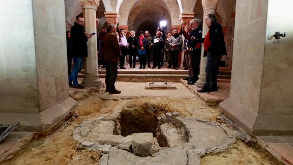 Menschen versammeln sich um eine freigelegte Öffnung in einer Kirche.